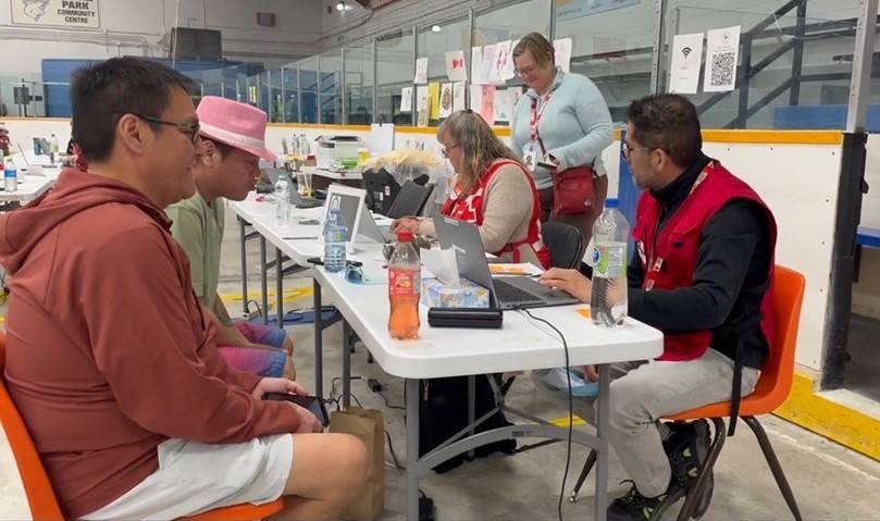 People sit around a table, those on right wearing Red Cross vests